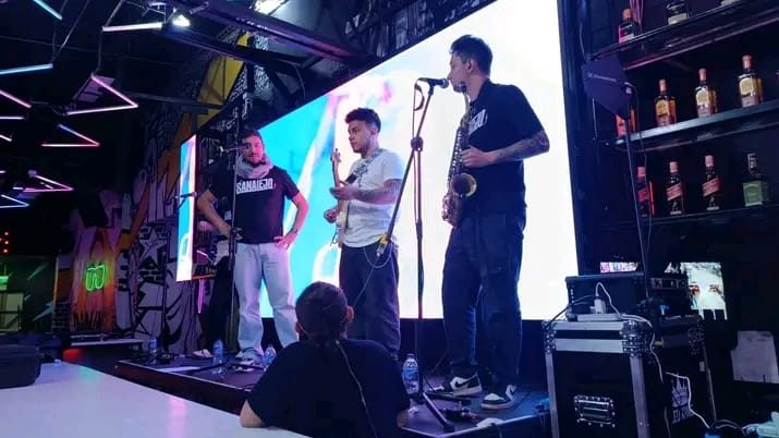 Banda en vivo tocando en un escenario con pantalla LED azul y público al frente