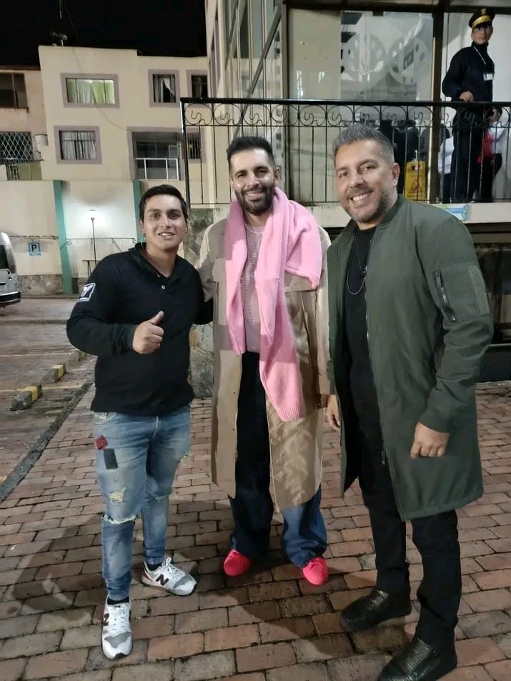 Tres personas posando juntas de noche al aire libre, con luces de fondo