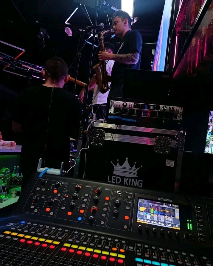 Consola profesional de sonido en primer plano y un saxofonista tocando en el escenario al fondo